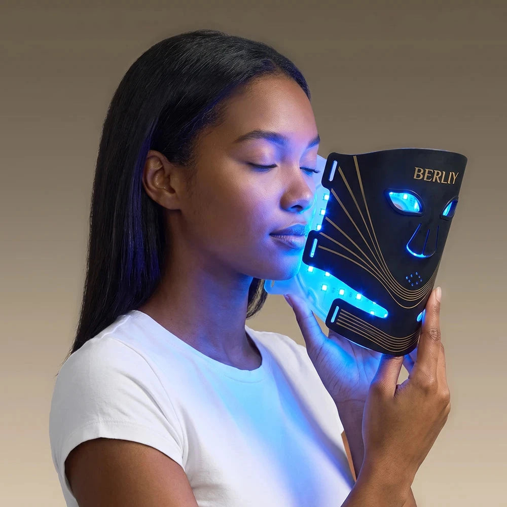 Woman holding the BERLIY face and neck mask close to her face with blue light illuminating her skin.