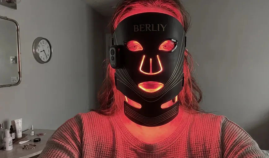 Emma wearing the black BERLIY LED face and neck mask with red light visible in the customer review section.